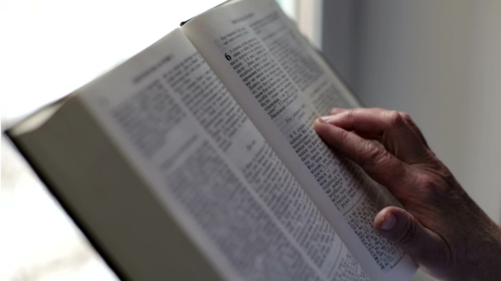 A hand traces the words in an open Bible